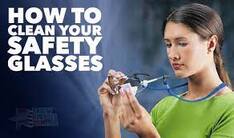 Woman cleaning safety glasses with a cloth, text reads "How to Clean Your Safety Glasses."| SpecSMART Eye Clinic Ikoyi