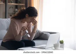 Woman experiencing eye strain while using a laptop, holding her glasses and rubbing her eyes| SpecSMART Eye Clinic Ikeja
